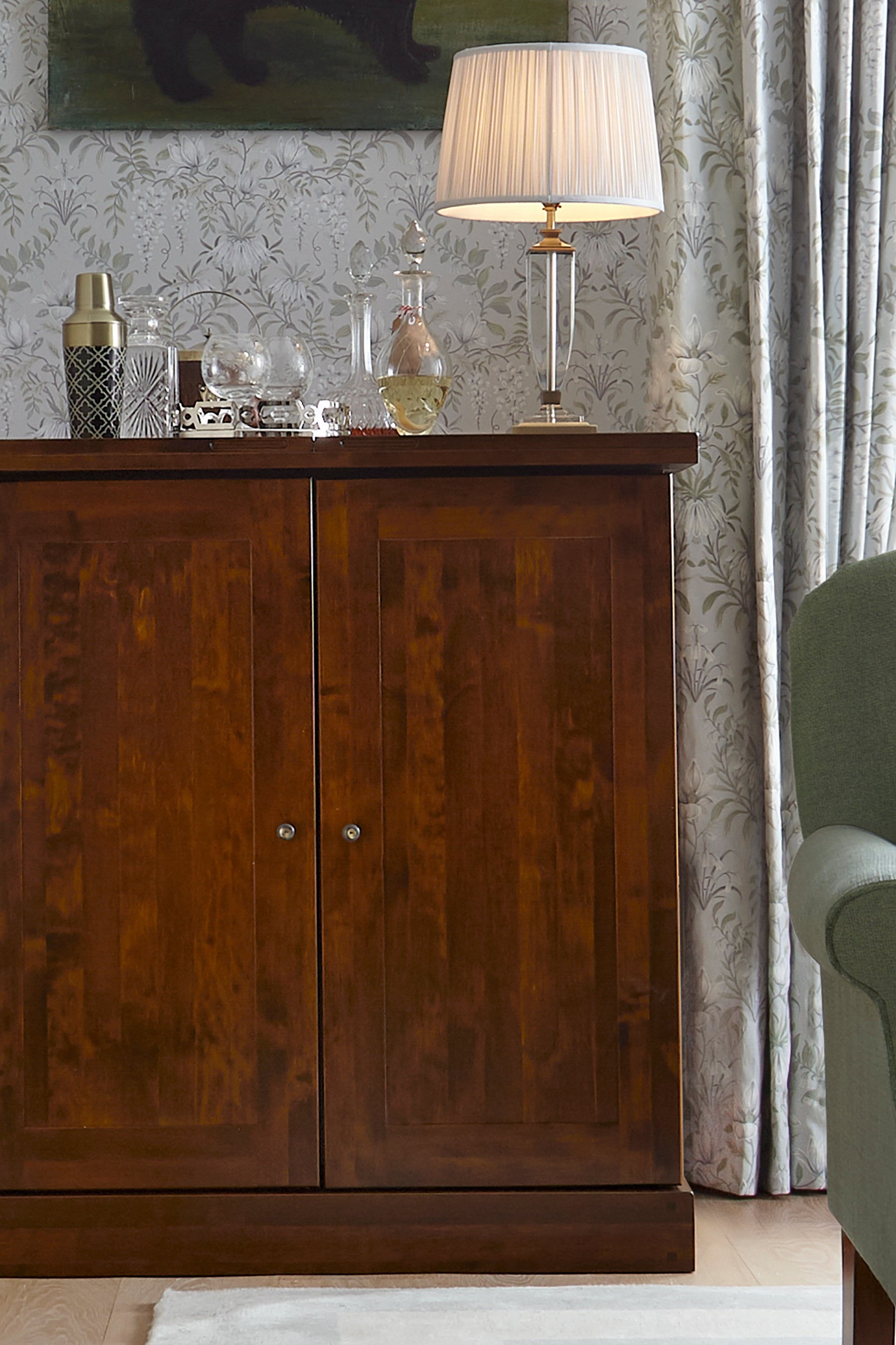 Wooden cabinet with a lamp and decorative items against a patterned wall.