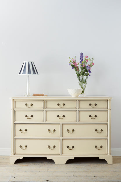 Beige dresser with drawers, lamp, and vase of flowers on a wooden floor.