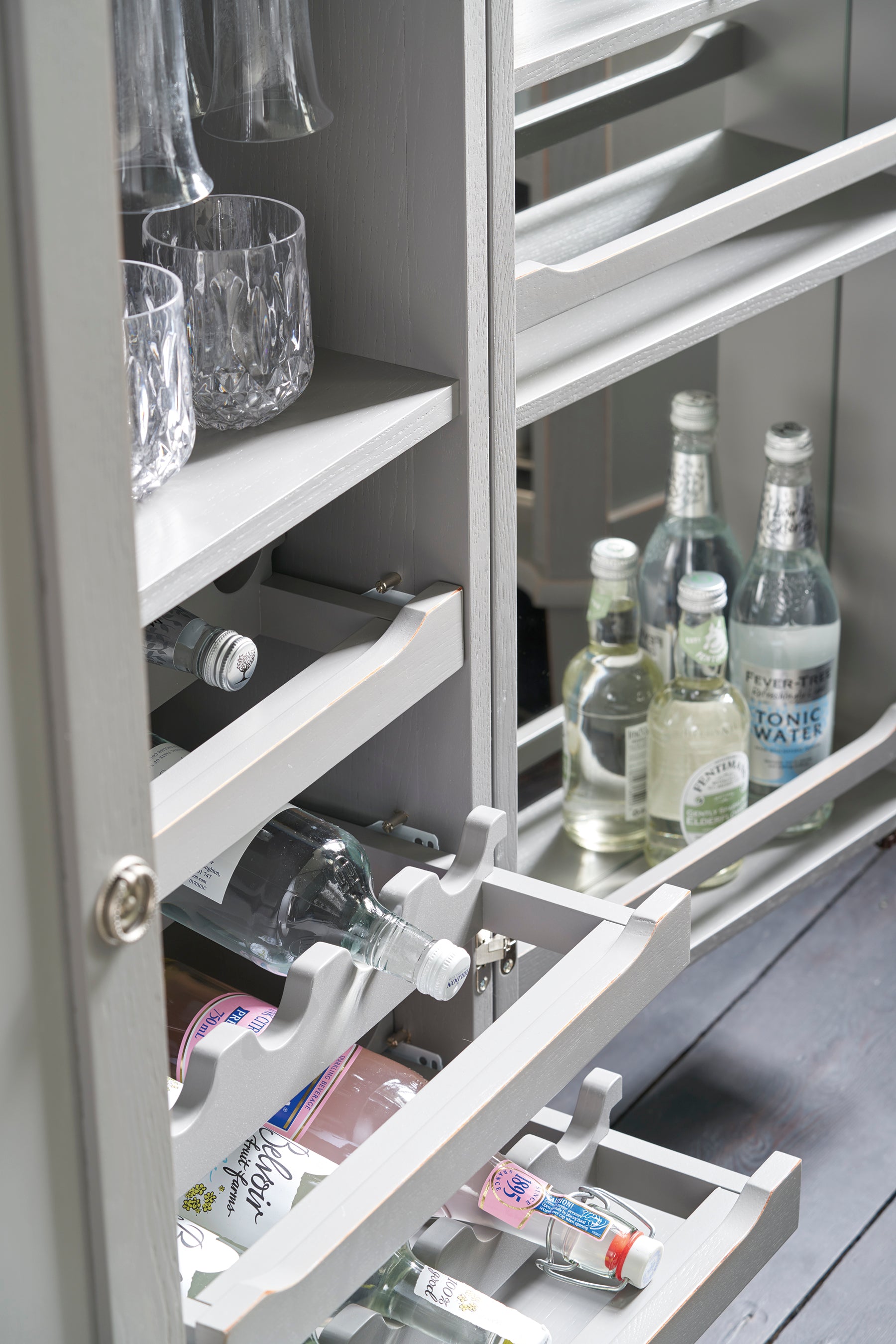 Grey drinks cabinet with open shelves containing bottles and glasses