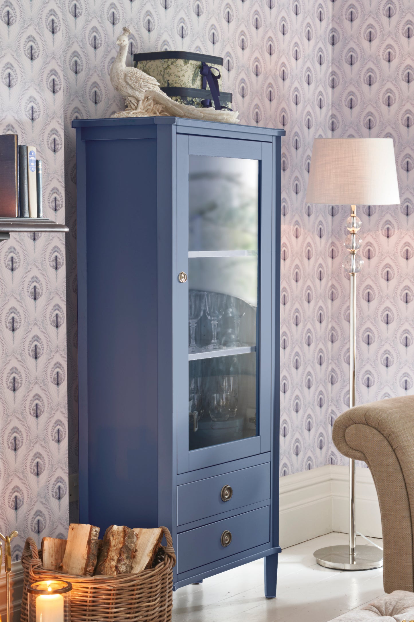 Blue glass-fronted cabinet against a patterned wallpaper wall with a lamp and decorative items.