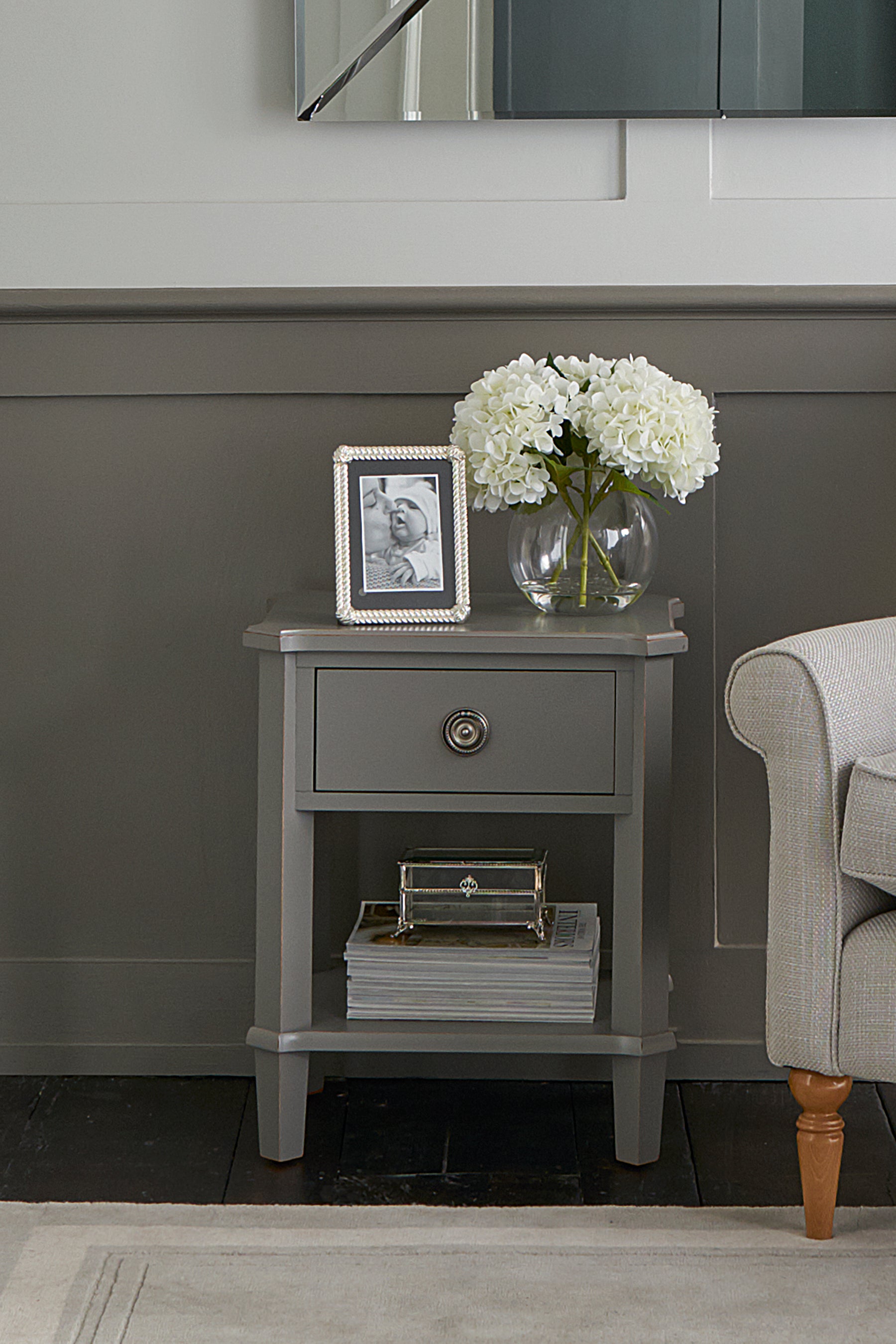 Gray side table with a vase of flowers and photo frame against a gray wall.