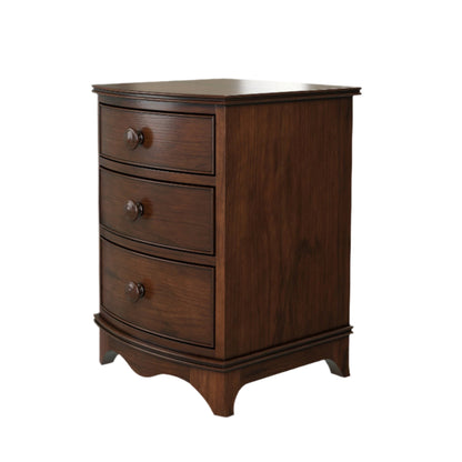 A right-hand corner angle view of a dark wooden 3-drawer bedside chest with a curved front and traditional design