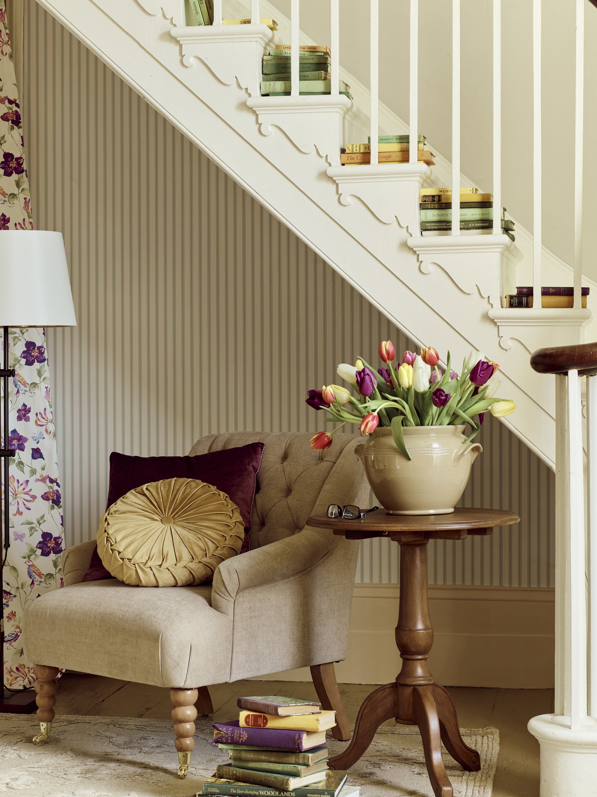 Living room with a beige armchair, wooden side table, and staircase with decorative items.