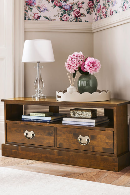Wooden side table with drawers, lamp, and flowers in a stylish room.