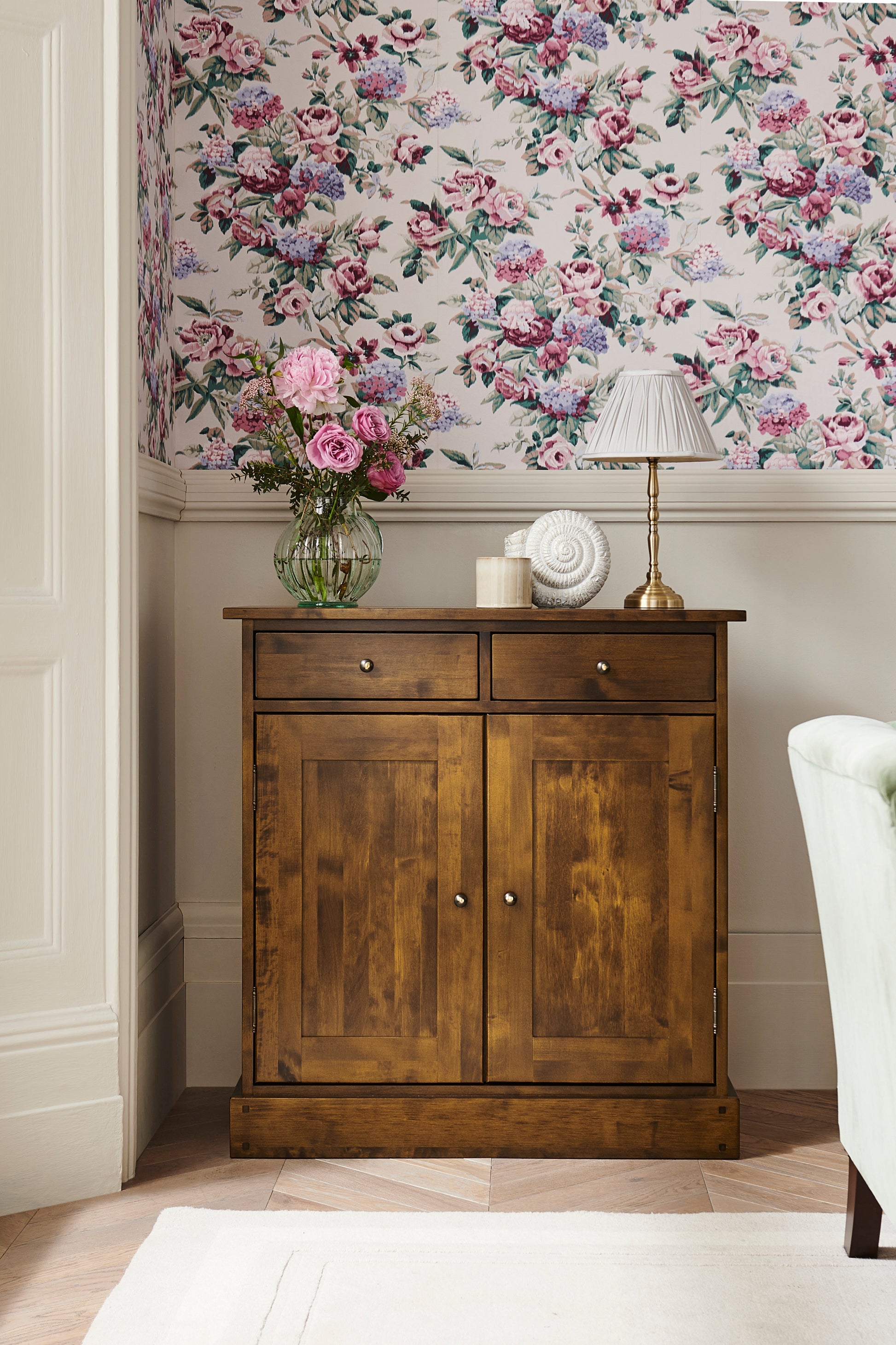 Wooden cabinet with floral wallpaper and decor in a corner.