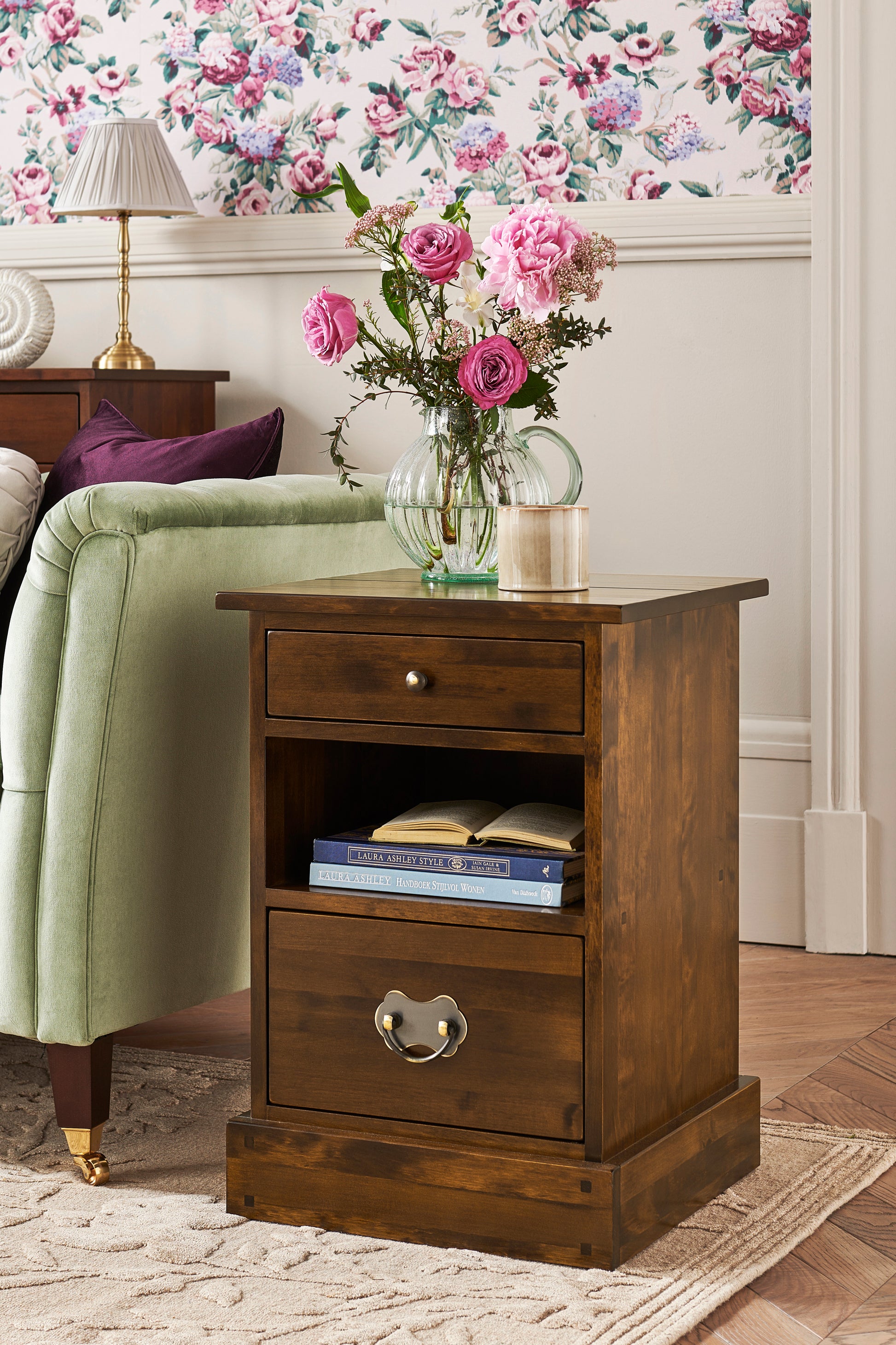 Wooden side table with a vase of flowers and books next to a green armchair.