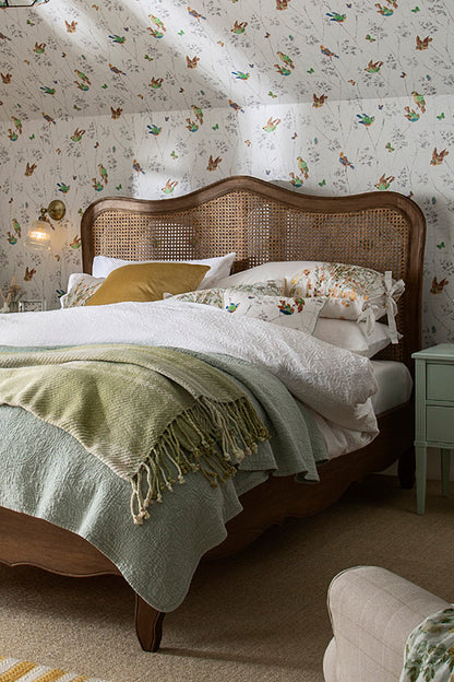 Bedroom with floral wallpaper, wooden bed, and green blanket