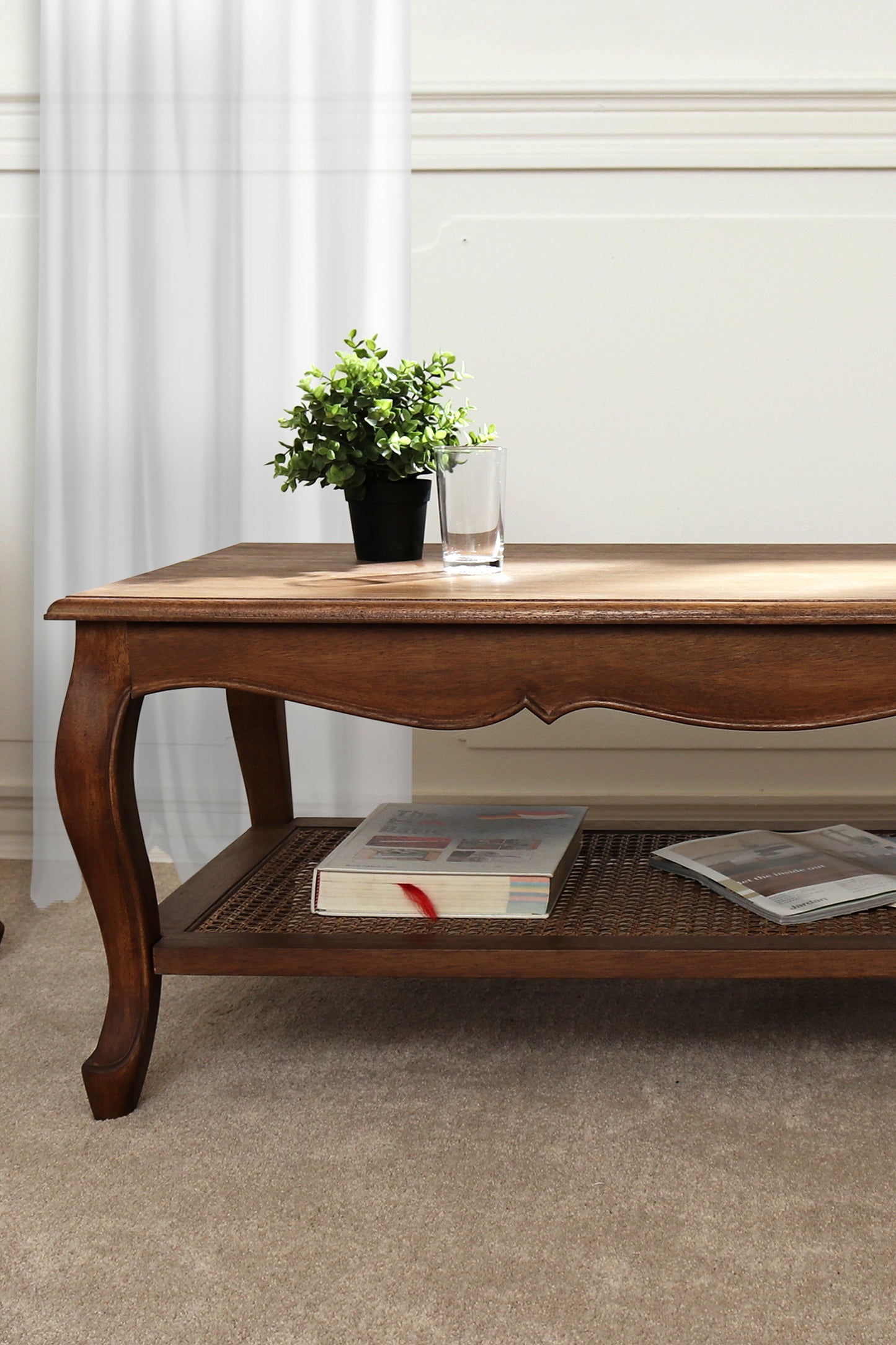 Wooden coffee table with a plant, books, and a glass on a carpeted floor.