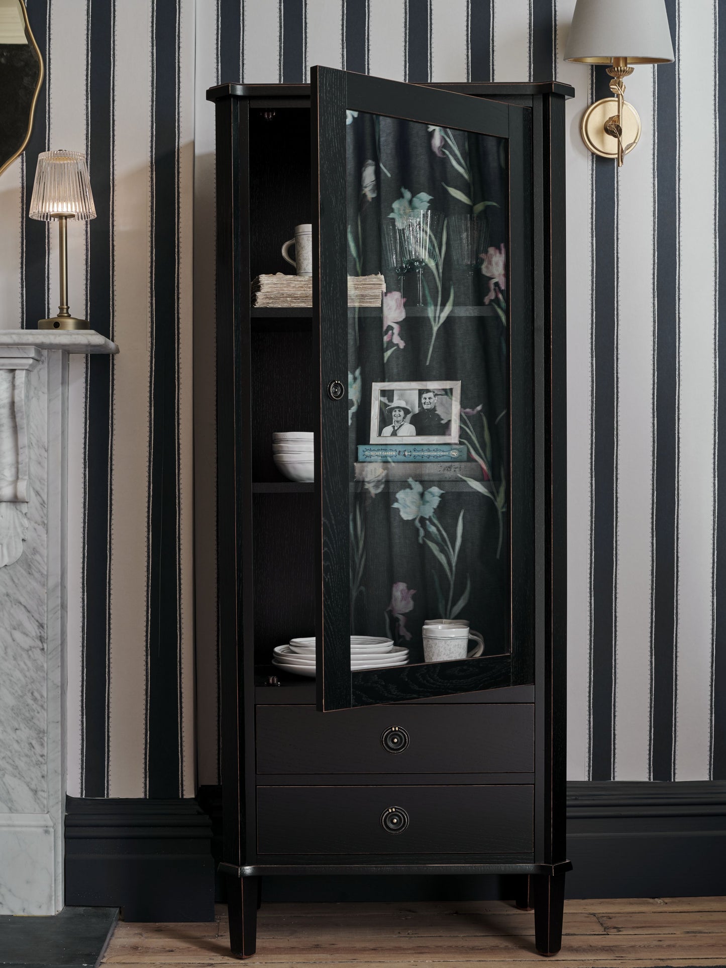 Black display cabinet with floral glass door against striped wallpaper