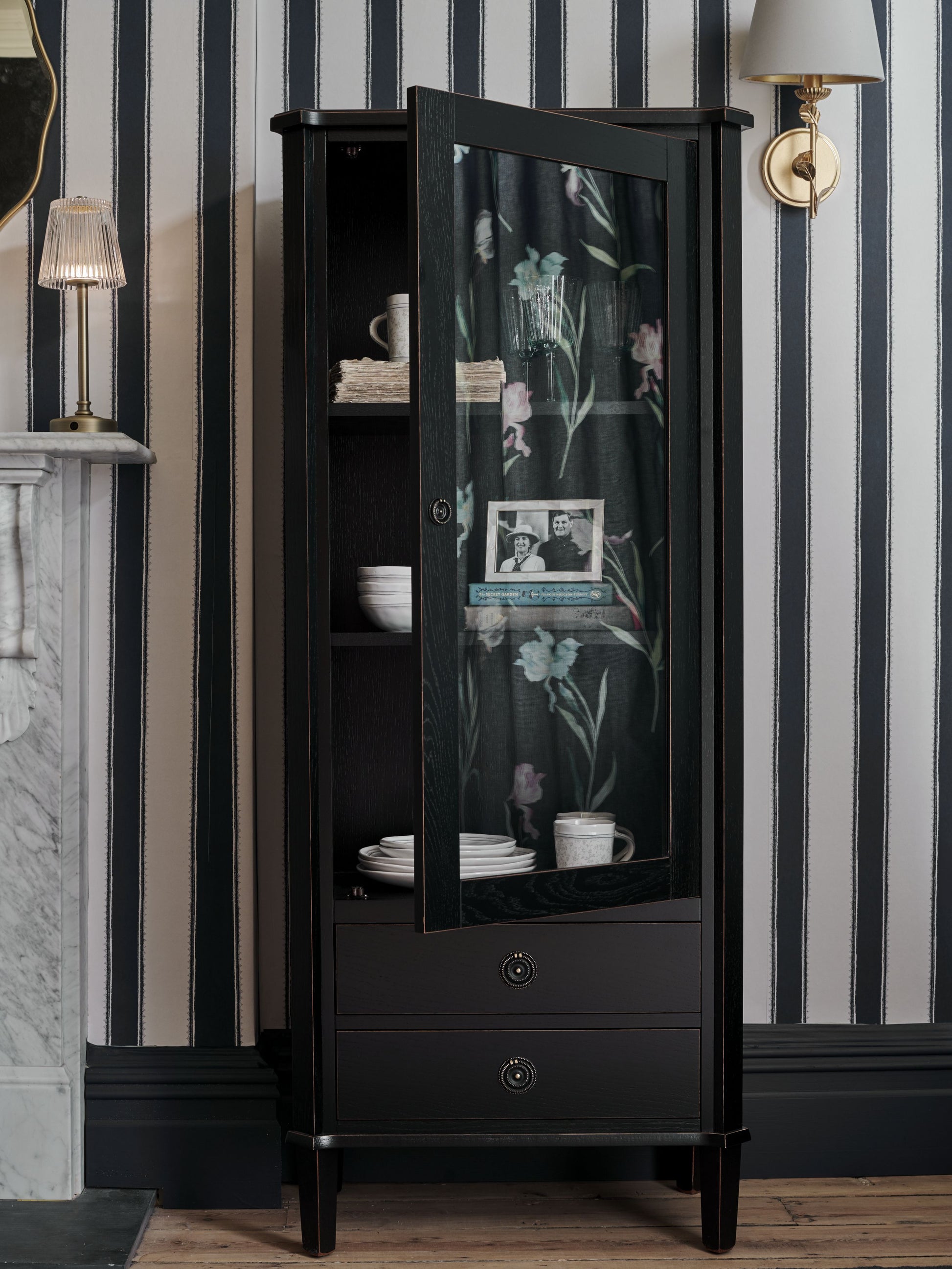 Black display cabinet with floral glass door against striped wallpaper