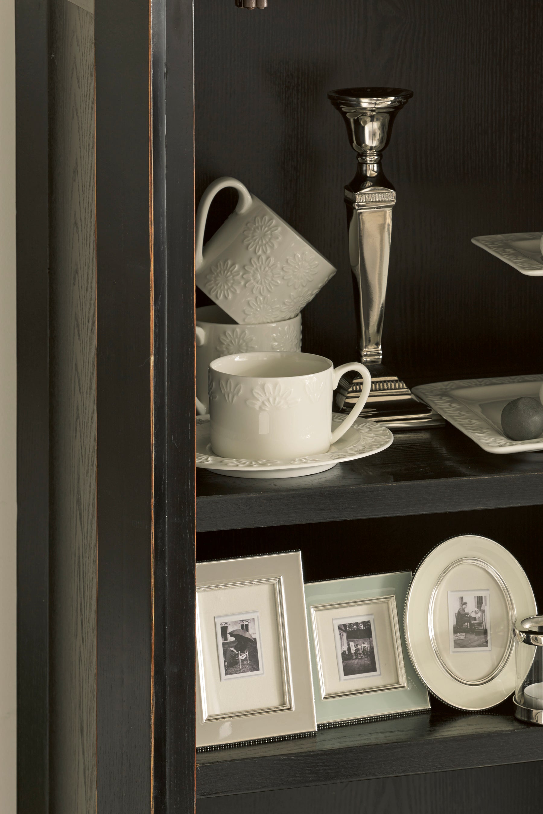 Decorative shelf with cups, plates, and framed pictures against a dark background