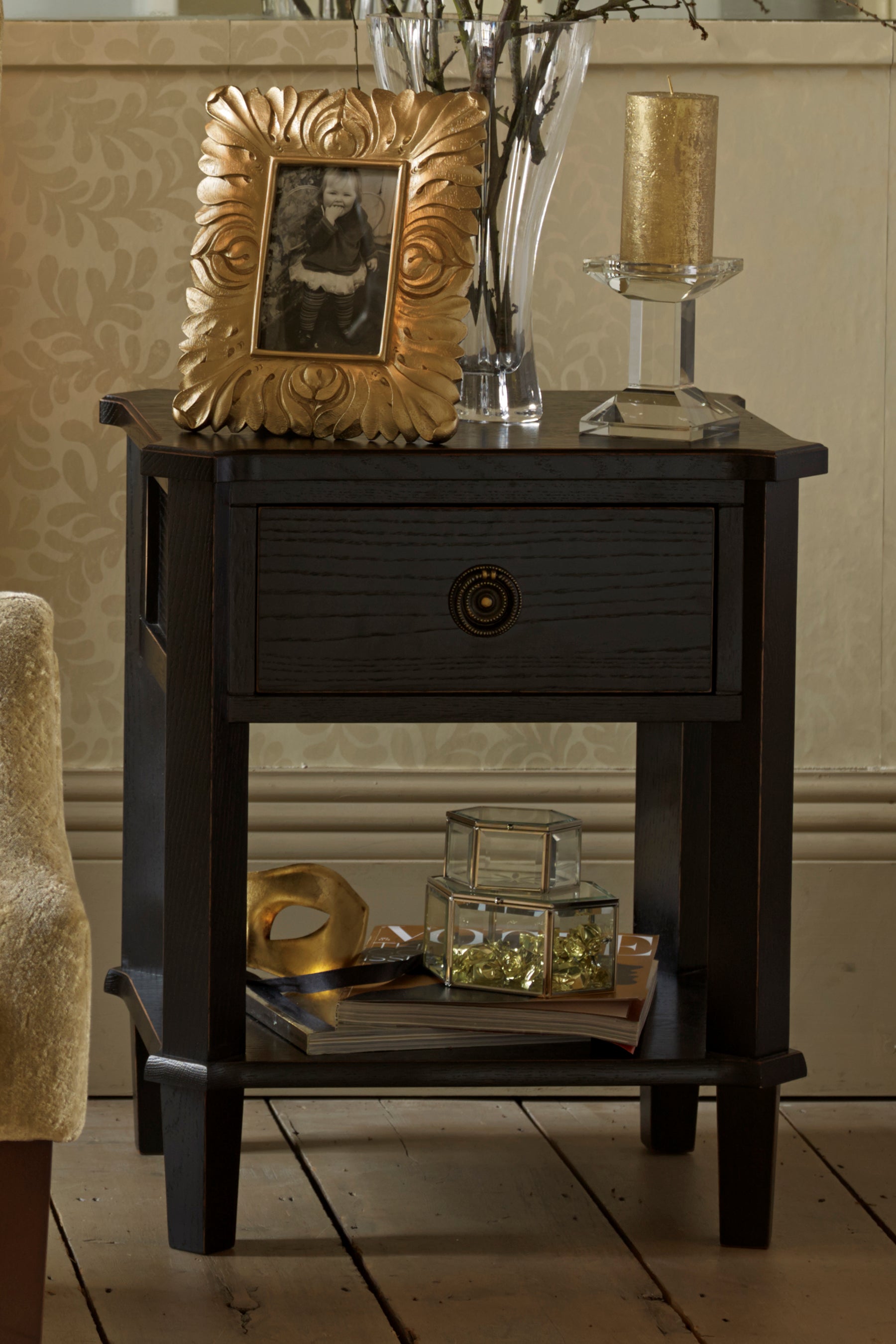 Dark wooden side table with gold frame, decorative items, and patterned wallpaper.