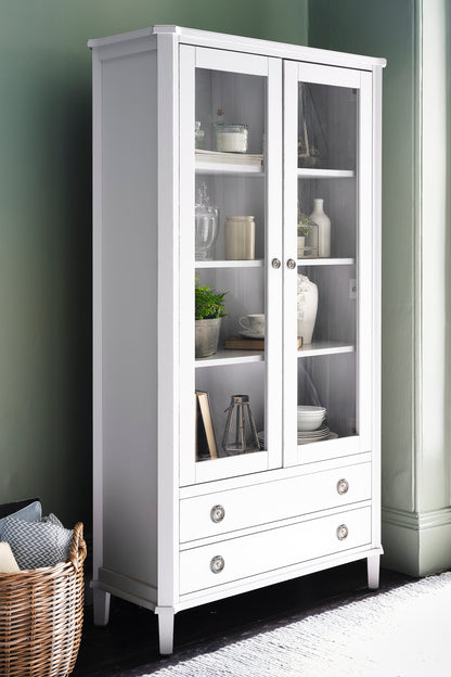 White display cabinet with glass doors and shelves against a green wall.