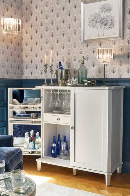 Pale grey drinks cabinet with drinks and glasses in a room with patterned wallpaper.