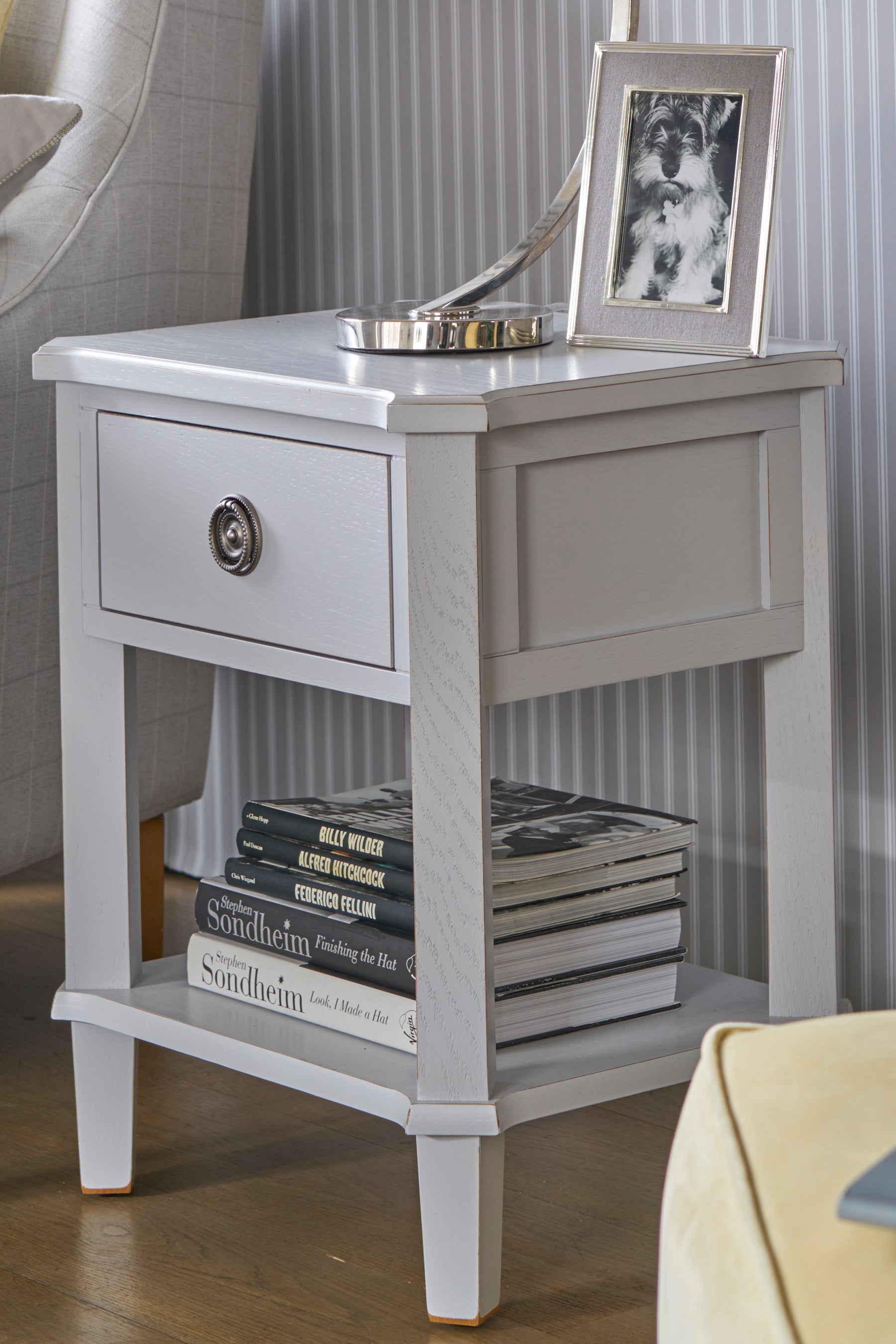 Gray side table with a drawer, books, and a framed picture on top.