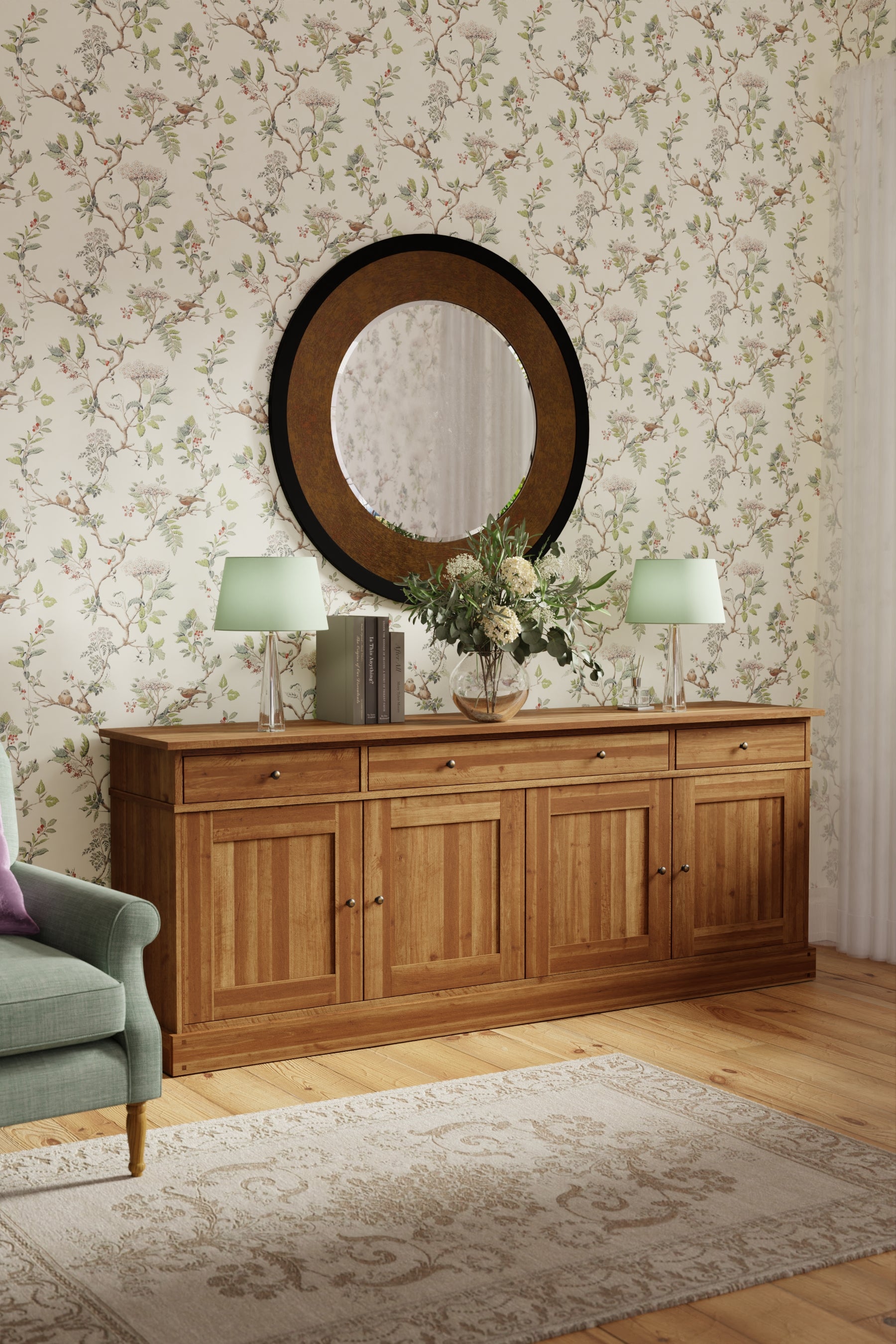 Honey coloured wooden sideboard with mirror and lamps in a room with floral wallpaper.