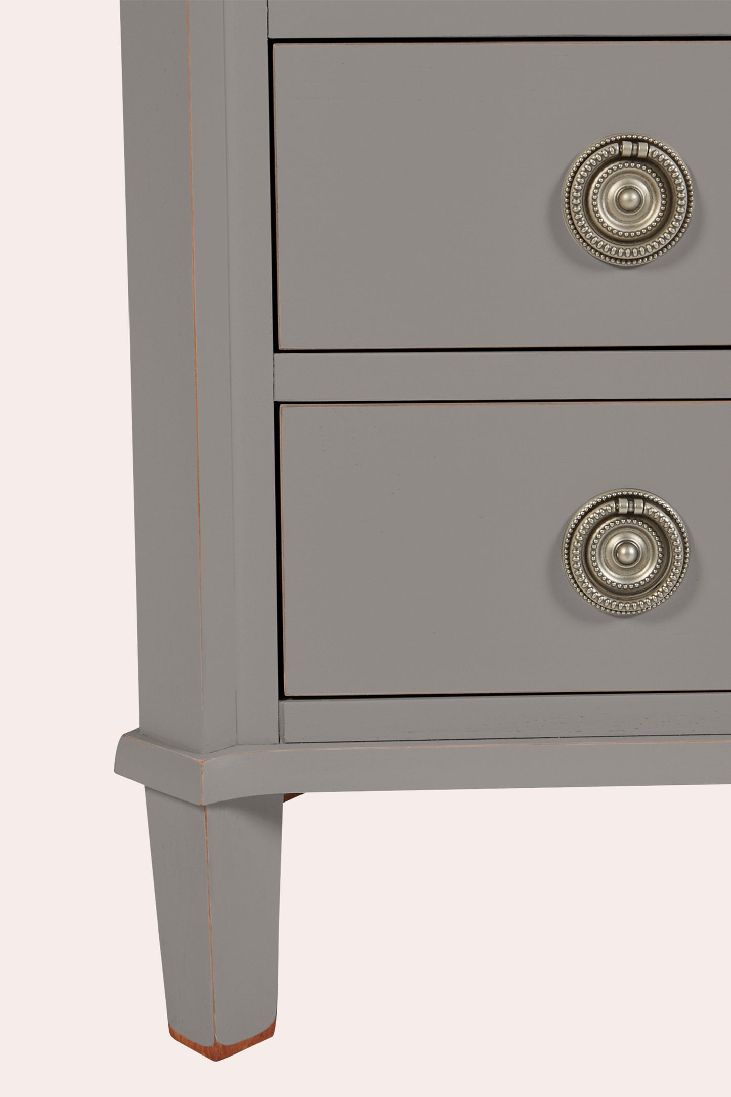 Gray dresser with two drawers and decorative knobs on a light pink background