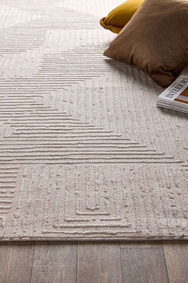 Textured beige rug on a wooden floor with a brown pillow and yellow item partially visible.