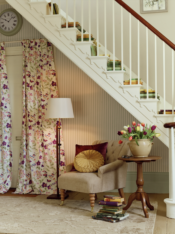 Living room with staircase, floral curtains, armchair, and side table.