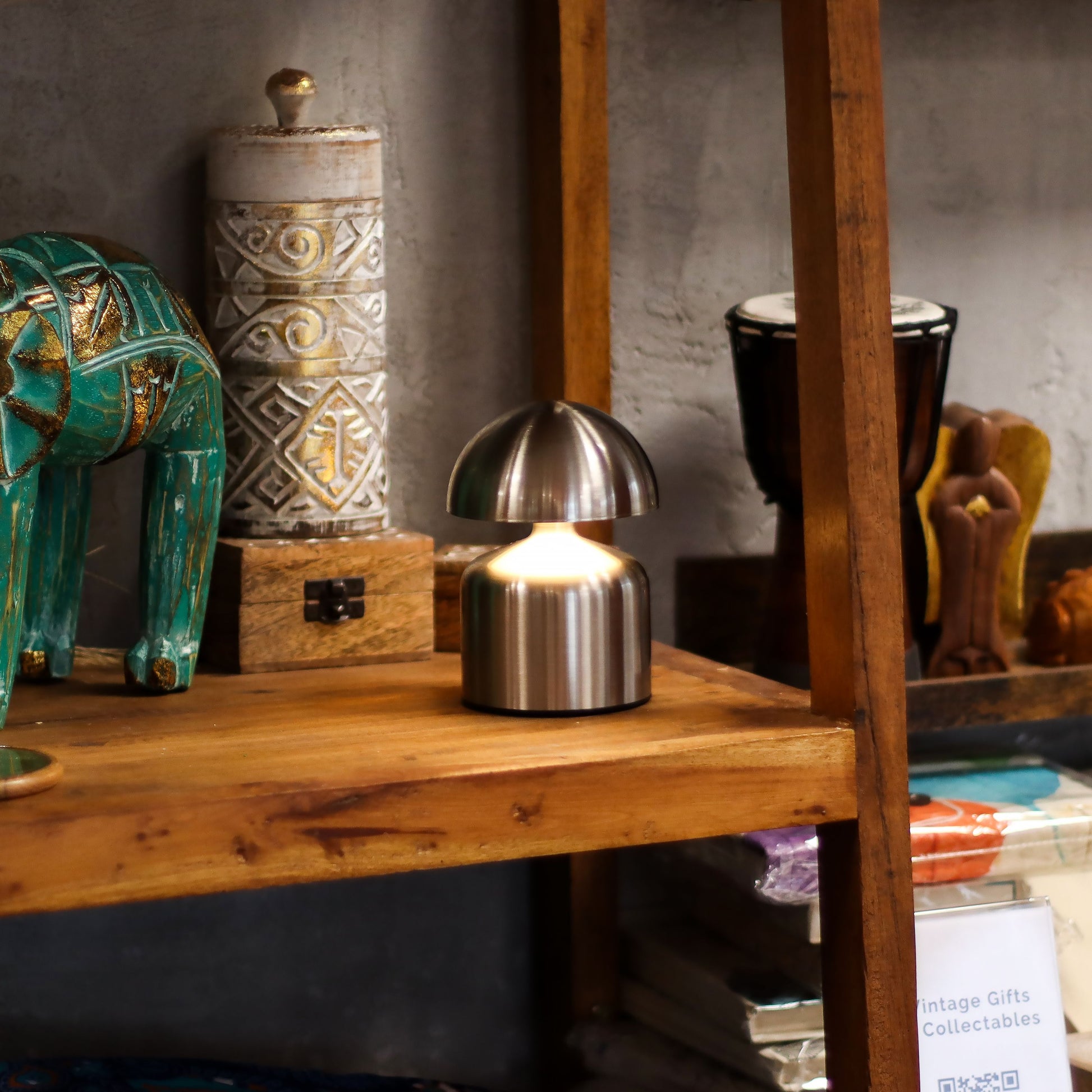 wooden Shelf with a silver metallic dome-shaped touch lamp surrounded by decorative items including a teal elephant and a textured cylindrical object.