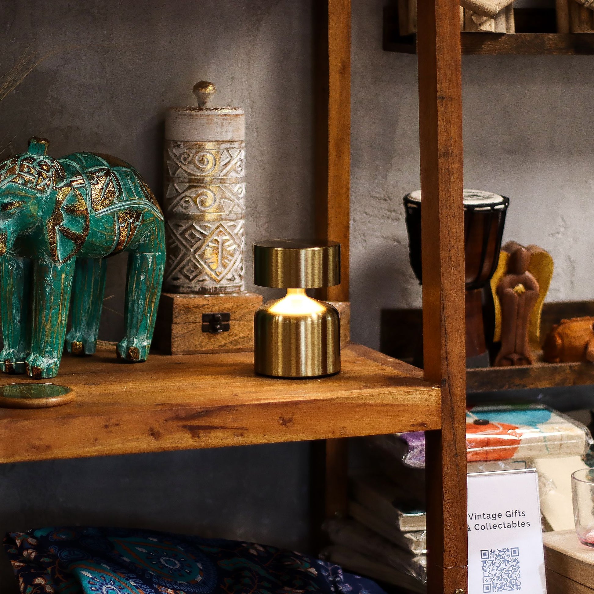 Gold touch lamp on a wooden shelf surrounded by other vintage-style decor items including a teal elephant, gold lamp, and other collectibles.