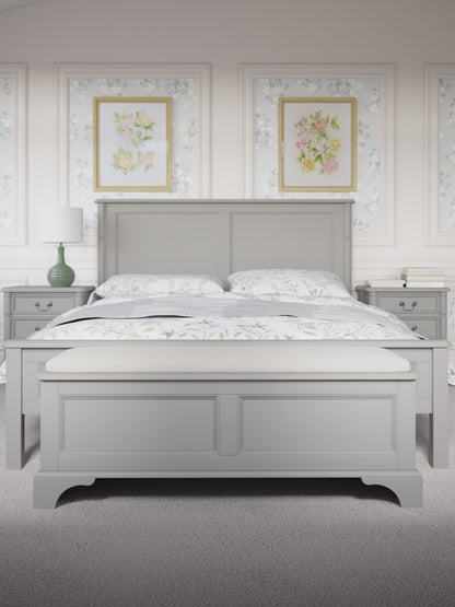 A dove grey blanket box with a cushioned top and wooden body, designed for storage and seating. The blanket box is situated at the end of a bed