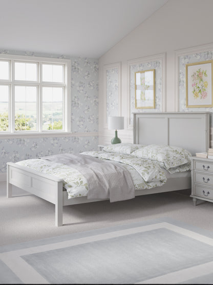 Dove grey wooden bed frame with a headboard and footboard, in a plain style with floral bedding and additional accessories
