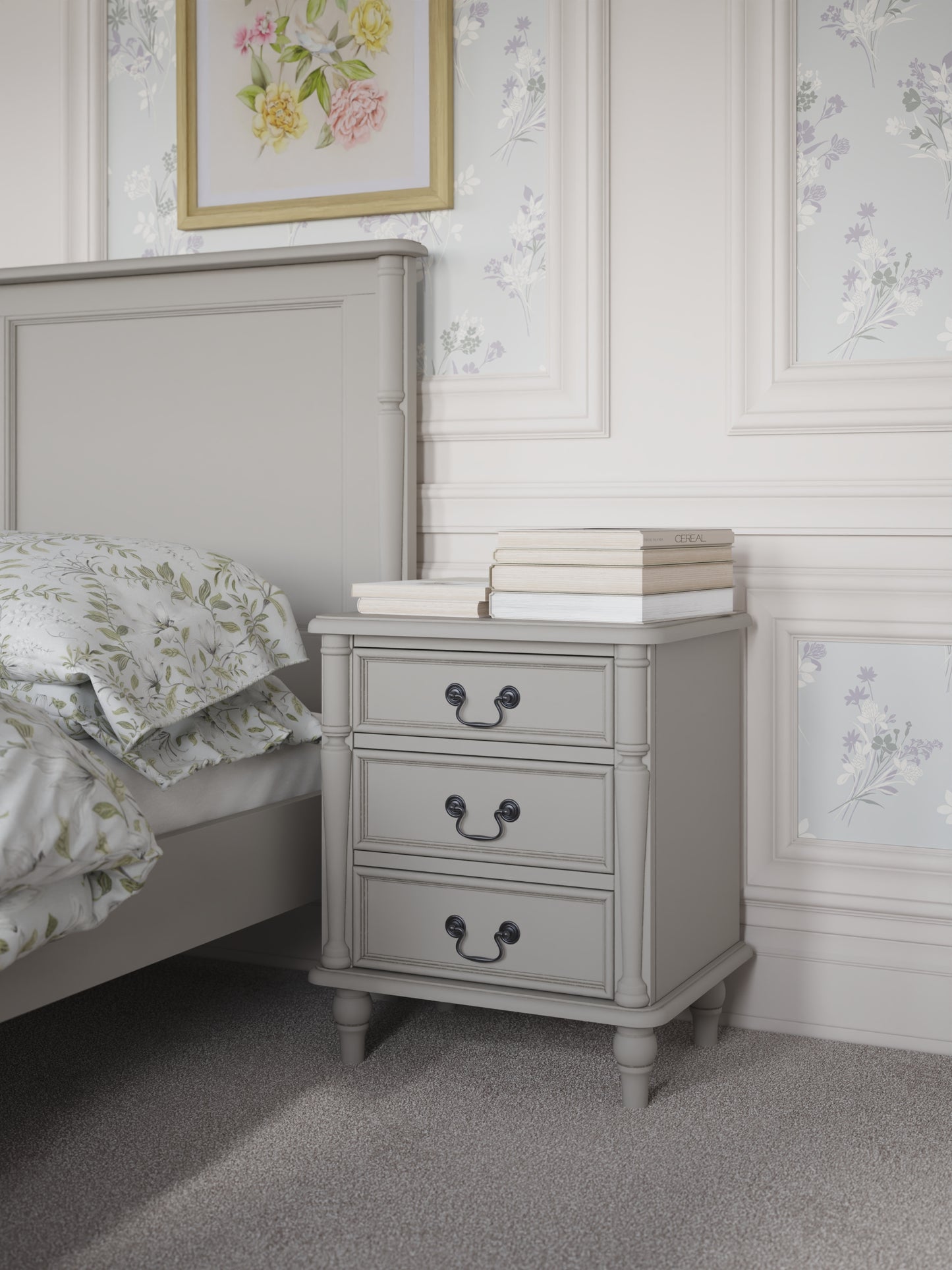 A dove grey 3-drawer bedside chest with traditional design and metal handles next to a bed with additional accessories