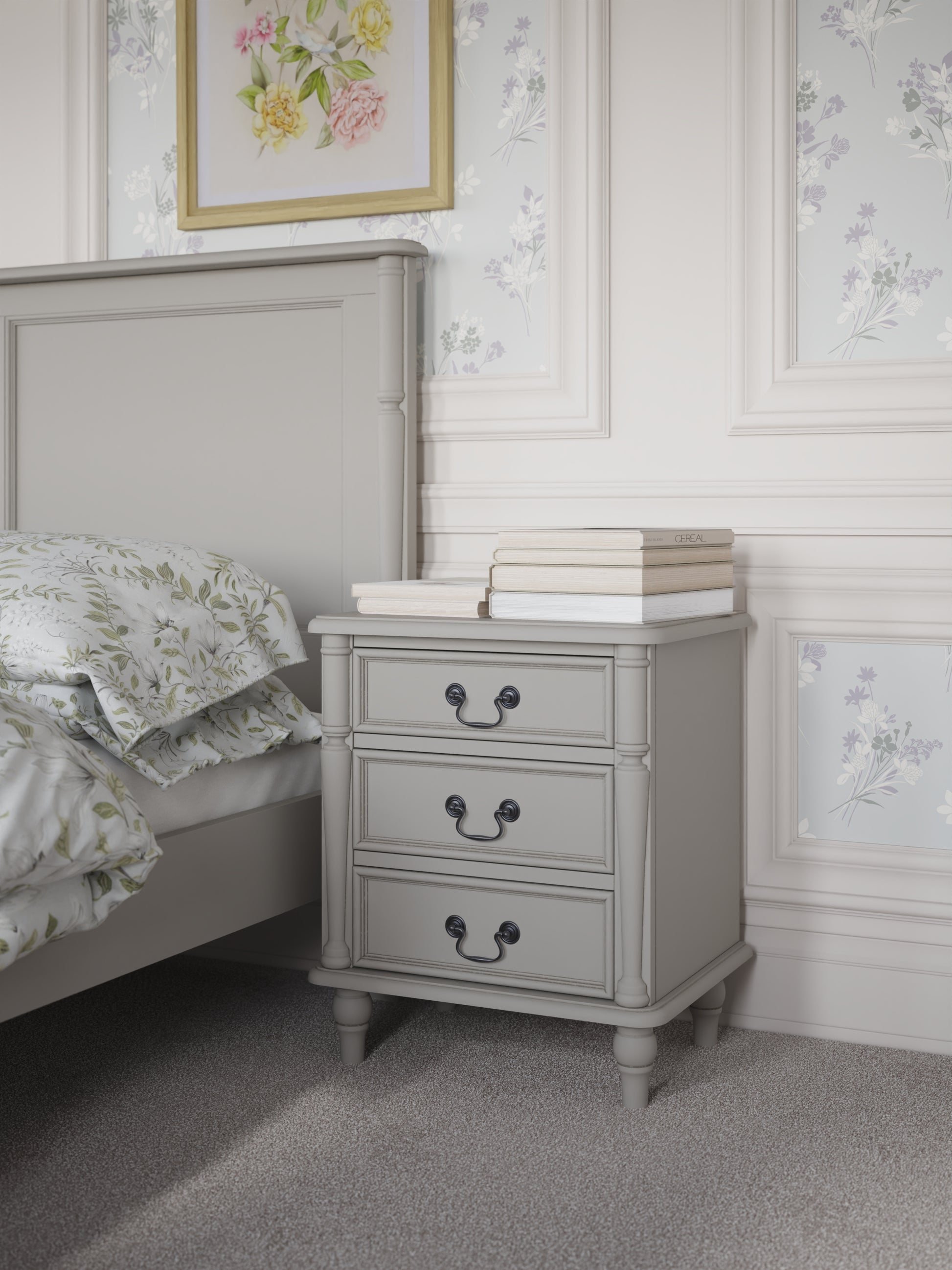 A dove grey 3-drawer bedside chest with traditional design and metal handles next to a bed with additional accessories