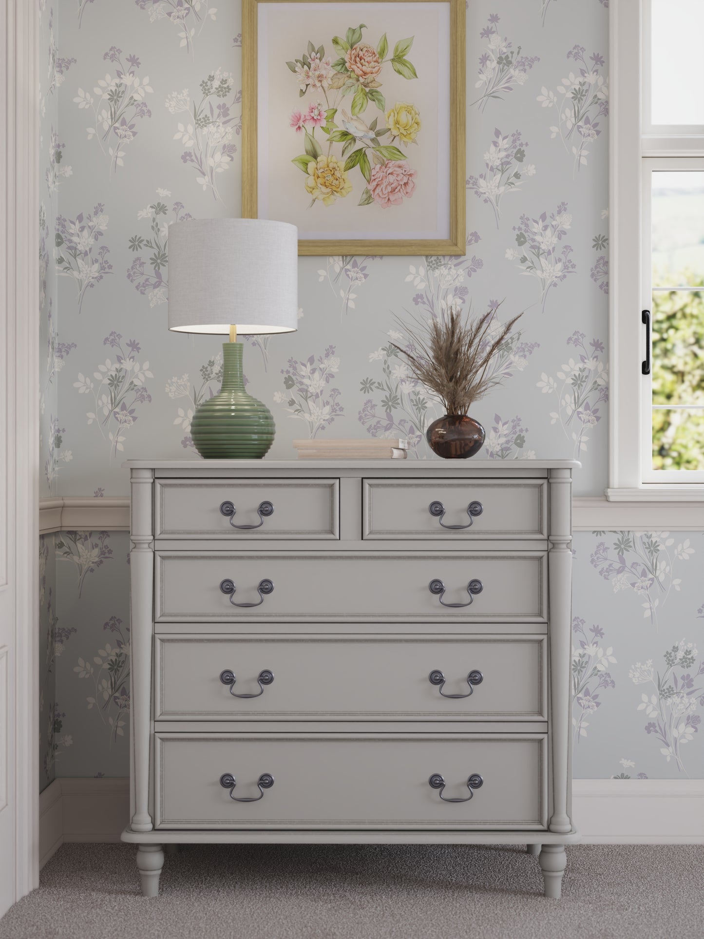 A dove grey chest of drawers with two smaller drawers on top and three larger ones below, each with a dark metal handle. Set against a floral wallpapered wall with a table lamp and plant on top.
