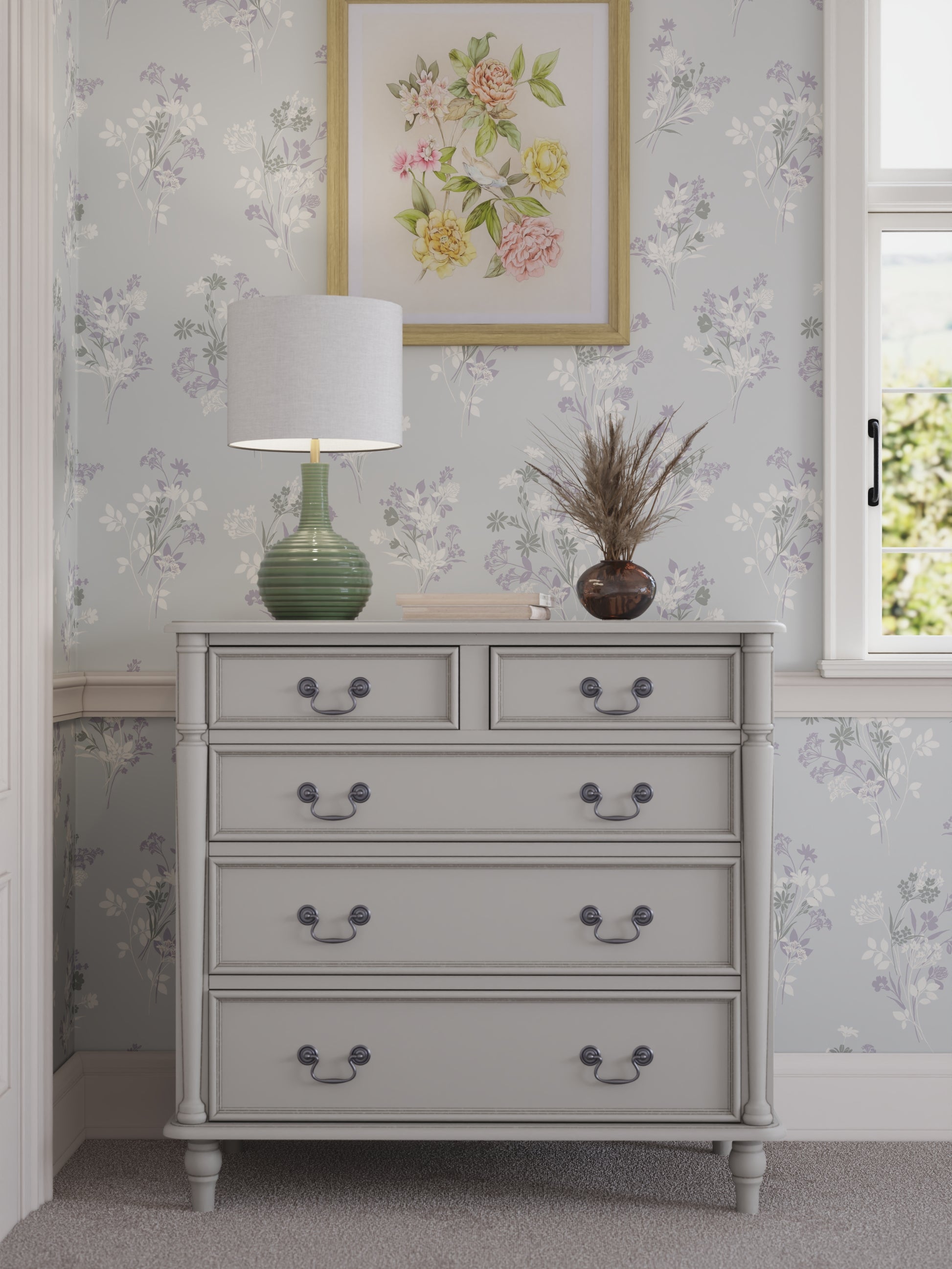 A dove grey chest of drawers with two smaller drawers on top and three larger ones below, each with a dark metal handle. Set against a floral wallpapered wall with a table lamp and plant on top.