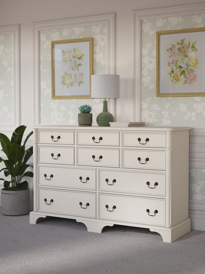 Ivory white dresser with multiple drawers in a room decorated with floral artwork and a plant.