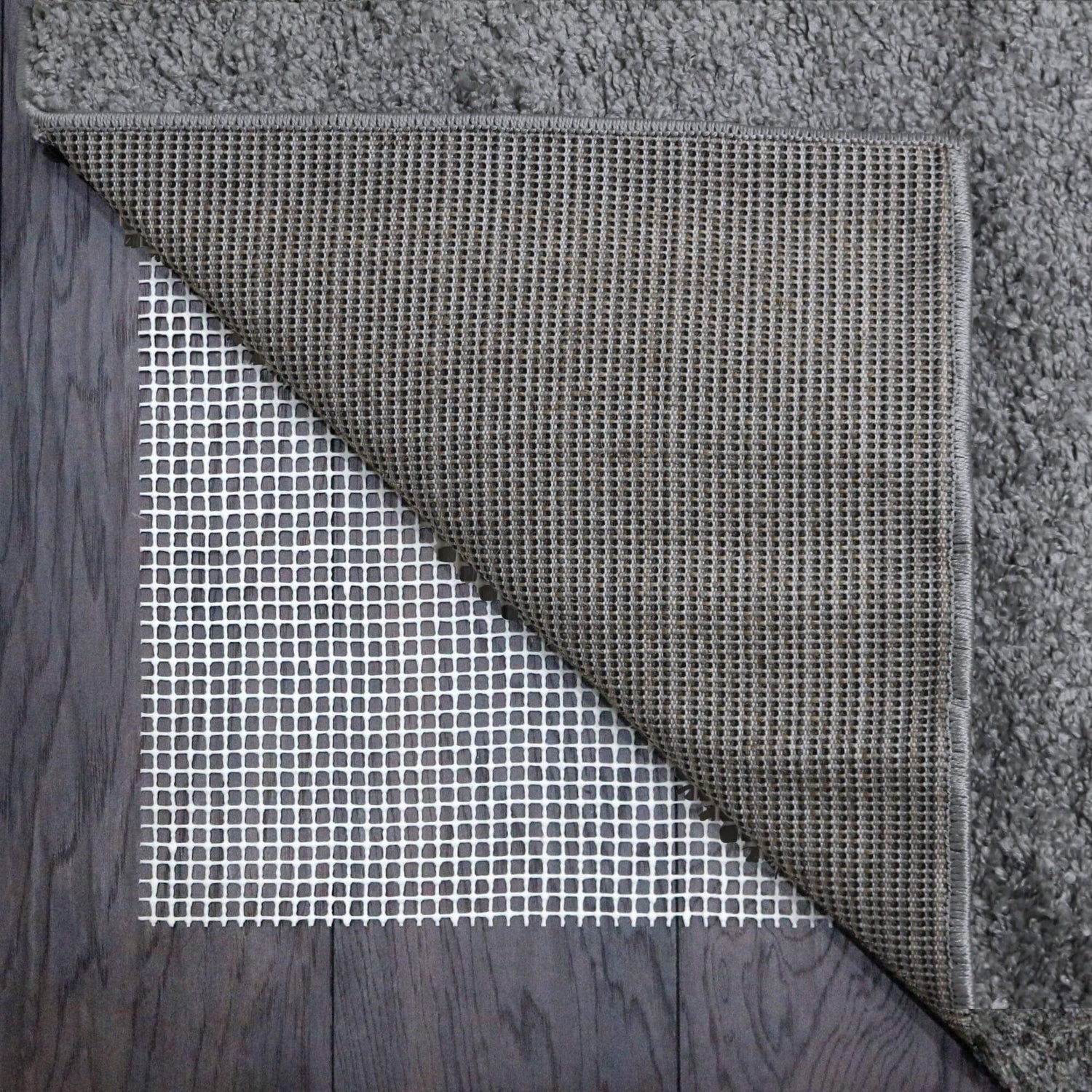 White mesh rug gripper with a grid pattern on a wooden floor underneath a grey rug