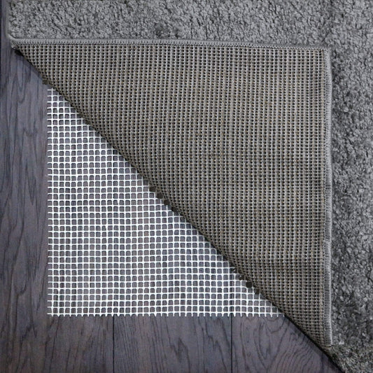 White mesh rug gripper with a grid pattern on a wooden floor underneath a grey rug