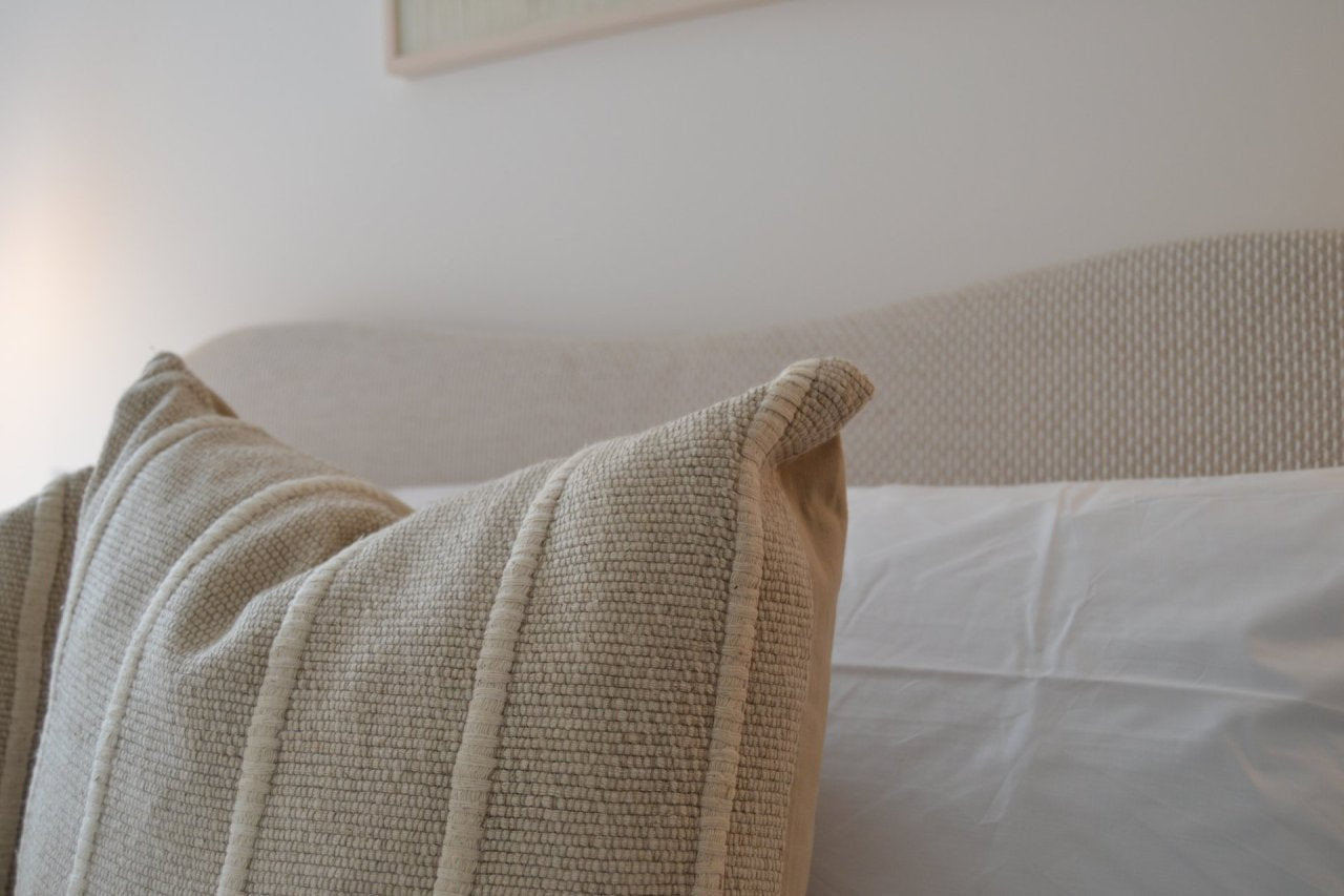 Textured beige pillow on a bed with a neutral headboard