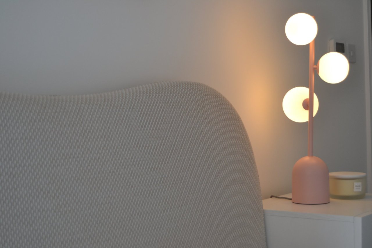 Modern pink table lamp on a nightstand next to a textured gray chair.