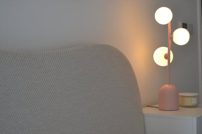 Modern pink table lamp on a nightstand next to a textured gray chair.